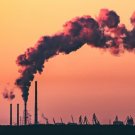 ciminiere con colonne di fumo su sfondo di complesso industriale